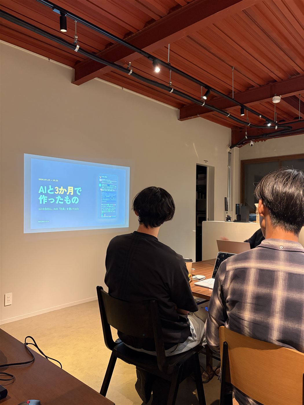 壁に映した発表の画面「AIと3か月で作ったもの」を見る参加者の後ろ姿